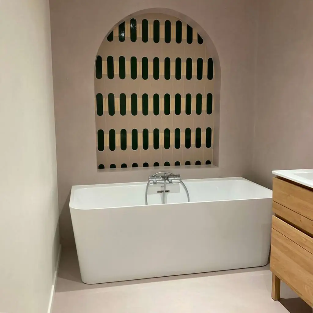 Zoom sur une salle de bain moderne associant béton ciré mural résistant à l'eau, meuble vasque en bois et baignoire blanche par Nuances Peinture Décoration.