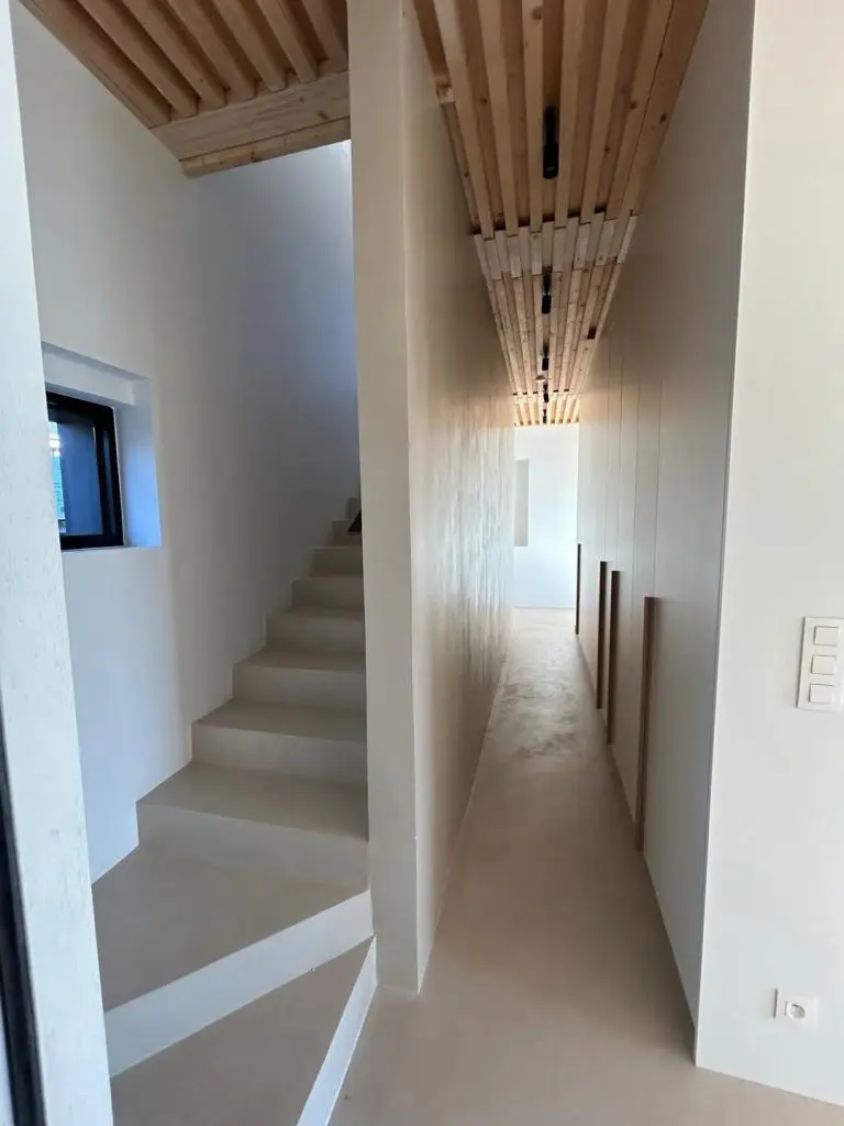 Aménagement intérieur moderne avec un revêtement de sol et un escalier design en béton ciré beige clair à Dinan par Nuances Peinture Décoration.