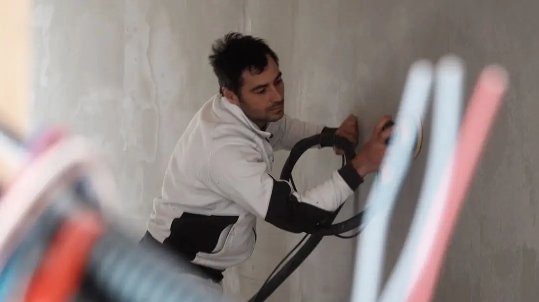 Un peintre décorateur en plein travail de ponçage de finition sur un mur en béton ciré dans un chantier à Dinan par Nuances Peinture Décoration