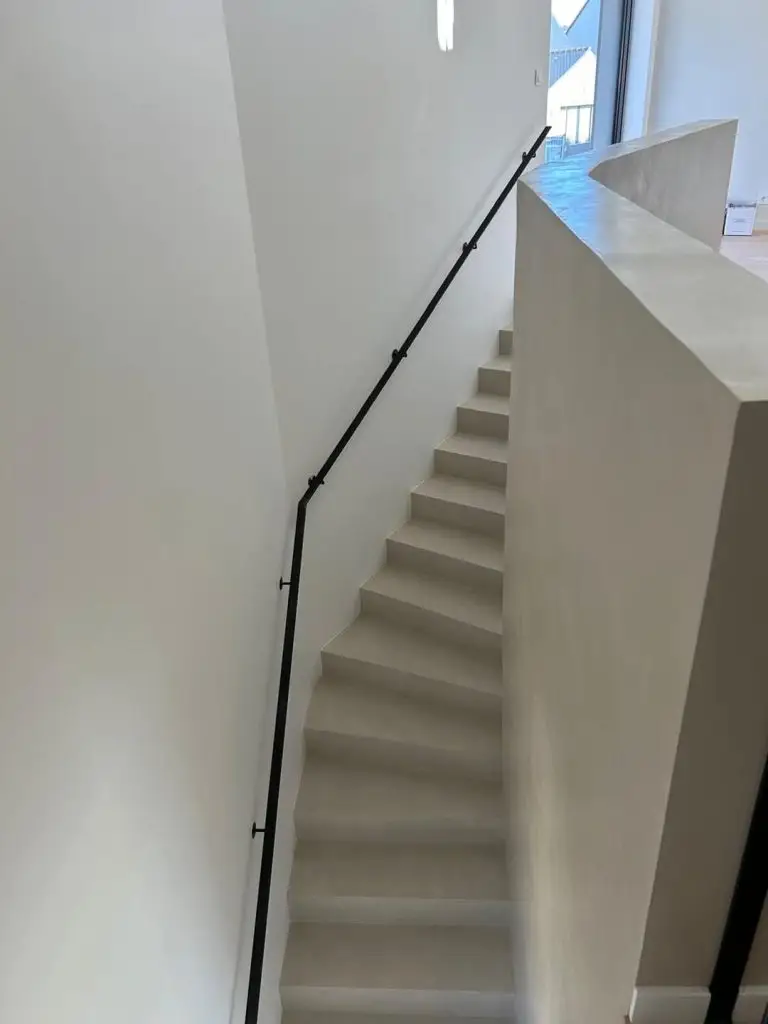 Vue plongeante sur un escalier tournant entièrement recouvert de béton ciré beige au rendu uniforme et épuré par Nuances Peinture Décoration.