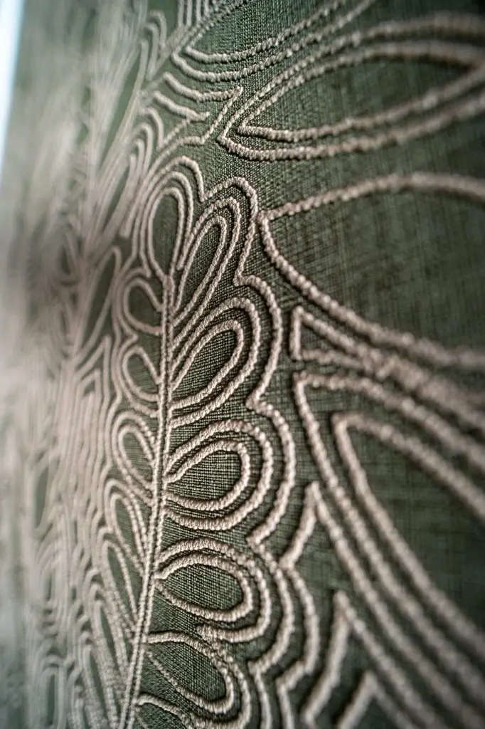 Détail de revêtements muraux texturés vert olive avec motifs brodés en relief, installé par Nuances peinture décoration