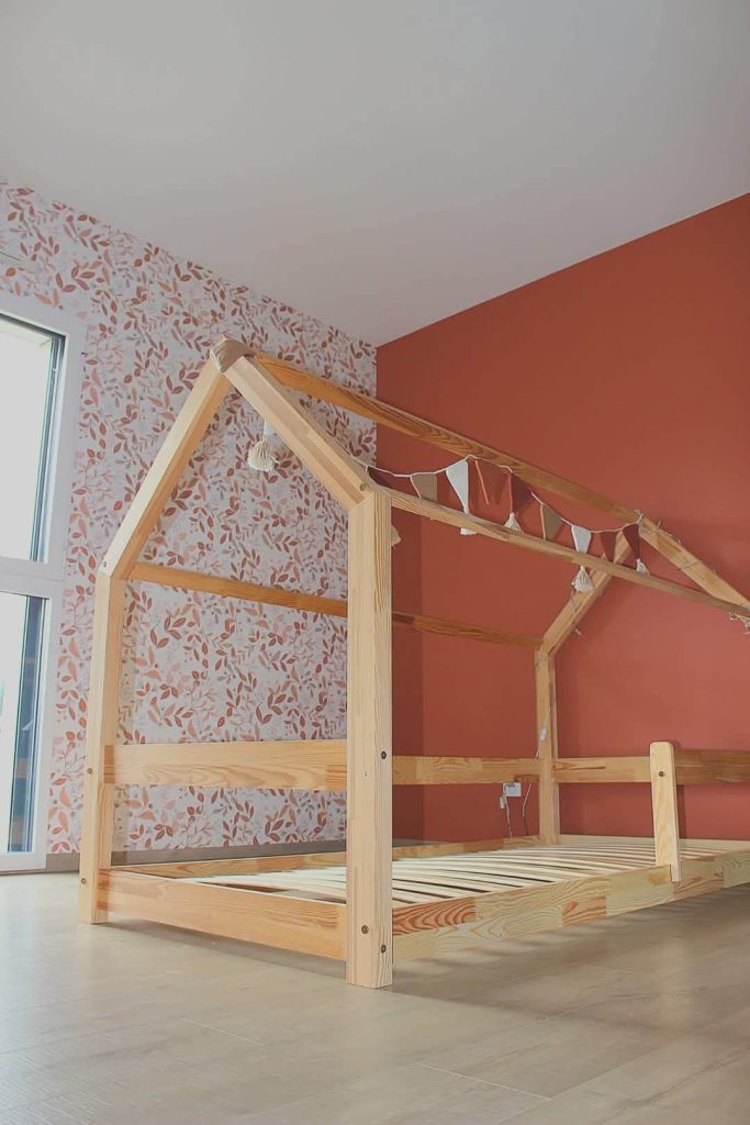 Aménagement d'une chambre d'enfant avec un mur peint en terracotta et pose de papier peint à motifs feuillage et peinture intérieure près de Dinan réalisé par Nuances Peinture Décoration