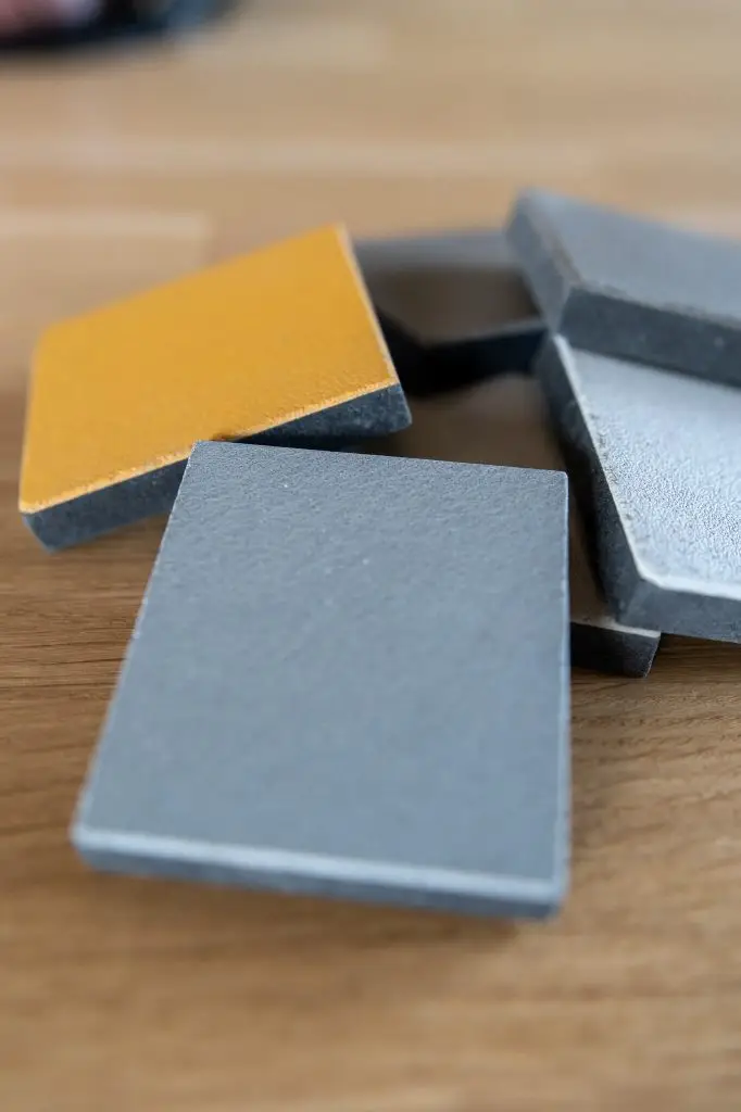 Sélection de plaques de béton ciré gris et ocre posées sur une table en bois pour apprécier le rendu de la matière par Nuances Peinture Décoration Dinan.