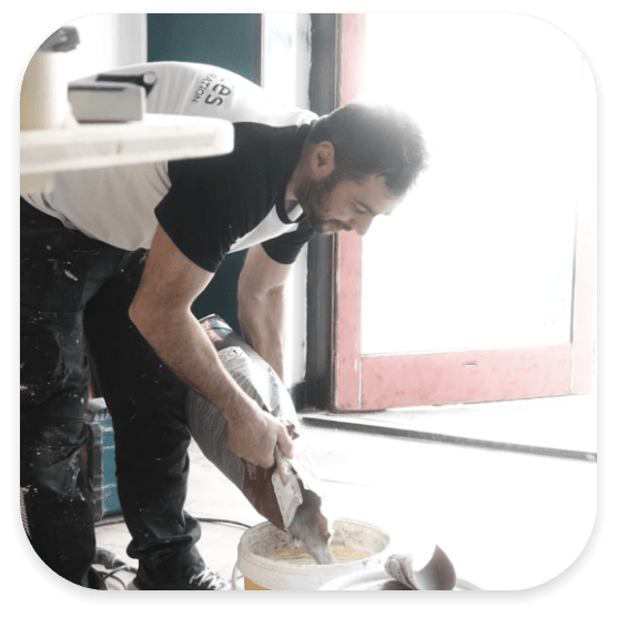 Artisan peintre en bâtiment préparant et mélangeant de l'enduit dans un seau sur un chantier de rénovation