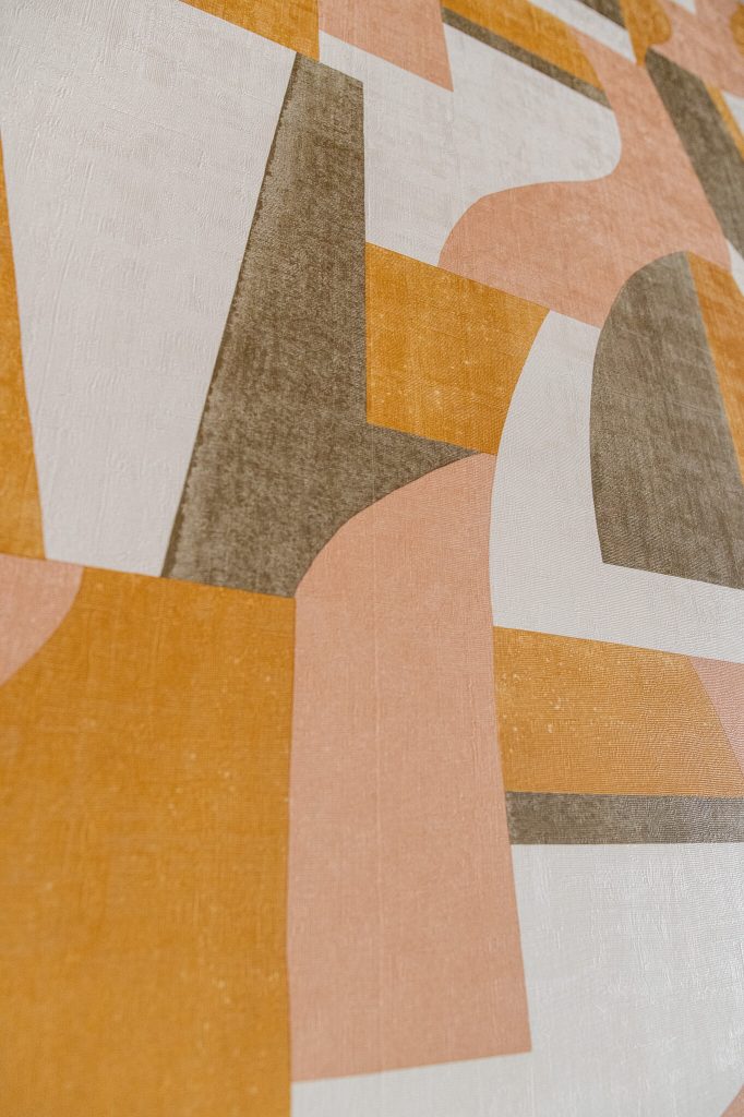 Révétements muraux - Gros plan sur un papier peint panoramique aux formes géométriques ocre, rose poudré et kaki posé par un artisan à Dinan par Nuances Peinture Décoration
