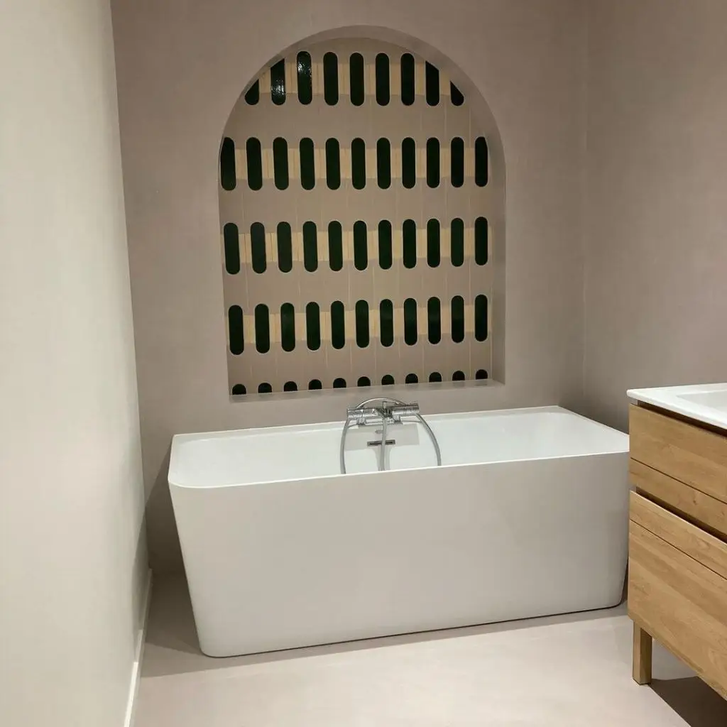 Décoration de salle de bain avec des murs en béton ciré rose poudré et une faïence graphique au-dessus d'une baignoire îlot à Dinan par Nuances Peinture Décoration.