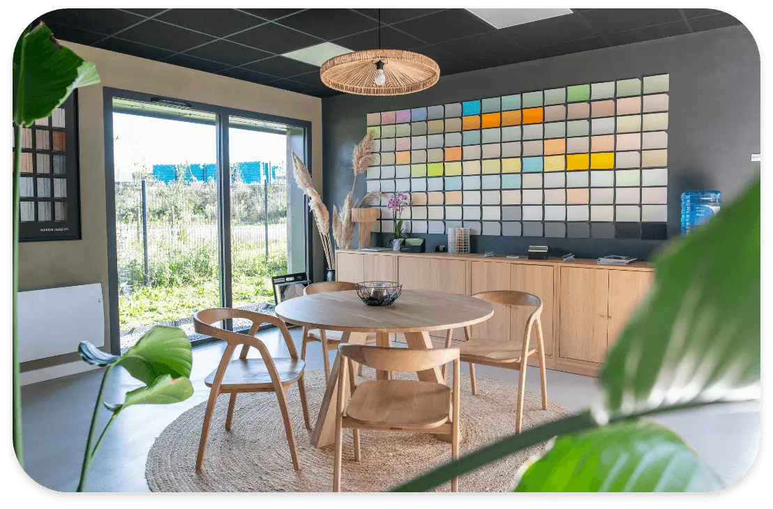 Showroom de décoration intérieure avec un grand mur de nuanciers de couleurs de peinture, une table en bois ronde et une décoration naturelle